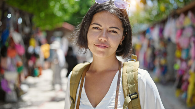 Young beautiful hispanic woman tourist wearing backpack standing at street market