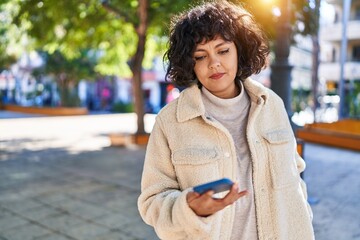 Young beautiful hispanic woman using smartphone with serious expression at park