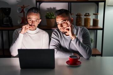 Homosexual couple using computer laptop mouth and lips shut as zip with fingers. secret and silent,...