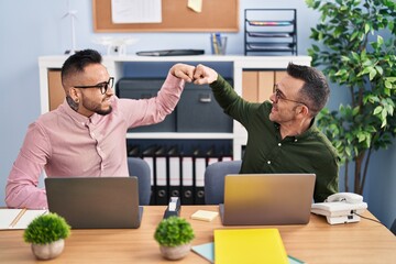 Two men business workers celebrate bump fists at office