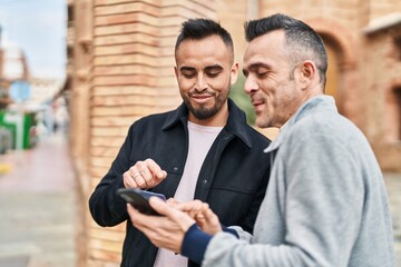 Two men couple smiling confident using smartphone at street