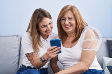 Mother and daughter using smartphone sitting on sofa at home