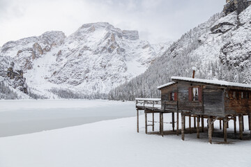 Wooden hut on stilts by the frozen Braies Lake surrounded by snowy mountains, Dolomites, Italy