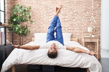 Young hispanic man smiling confident lying on bed with legs raised up at bedroom
