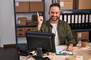 Middle age caucasian man working at small business ecommerce wearing headset smiling happy pointing with hand and finger to the side