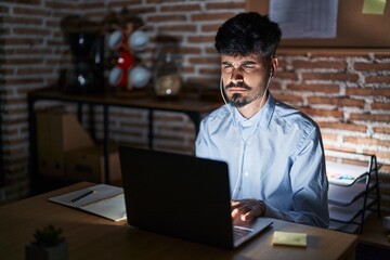 Young hispanic man with beard working at the office at night skeptic and nervous, frowning upset because of problem. negative person.