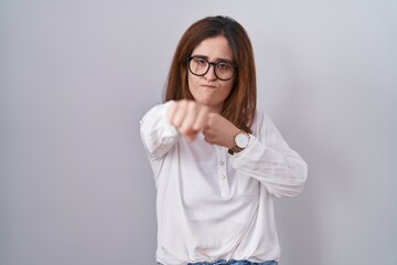 Brunette woman standing over white isolated background punching fist to fight, aggressive and angry...