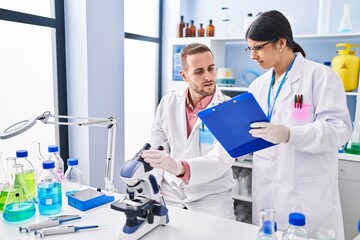 Man and woman wearing scientists uniform using microscope at laboratory