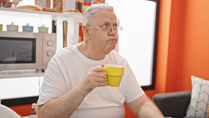 Middle age grey-haired man drinking coffee sitting on table at dinning room