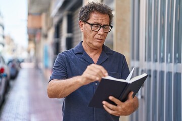 Middle age man reading book with relaxed expression at street