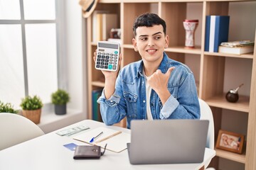 Fototapeta premium Non binary person calculating money savings pointing thumb up to the side smiling happy with open mouth