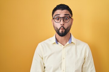 Obraz premium Hispanic young man wearing business clothes and glasses making fish face with lips, crazy and comical gesture. funny expression.