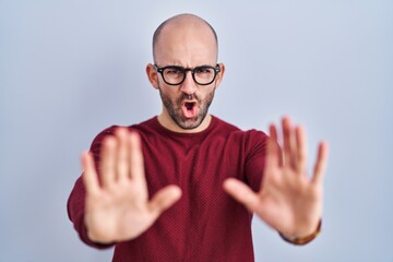 Fototapeta premium Young bald man with beard standing over white background wearing glasses doing stop gesture with hands palms, angry and frustration expression