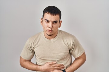 Young arab man wearing casual t shirt with hand on stomach because indigestion, painful illness feeling unwell. ache concept.