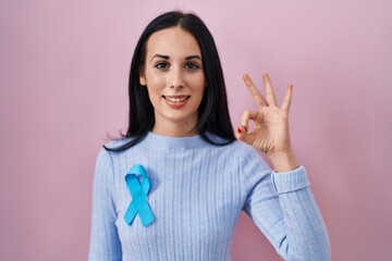Hispanic woman wearing blue ribbon doing ok sign with fingers, smiling friendly gesturing excellent...