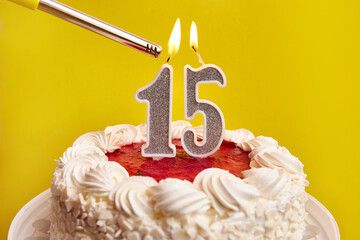 A candle in the form of the number 15, stuck in a festive cake, is lit. Celebrating a birthday or a...