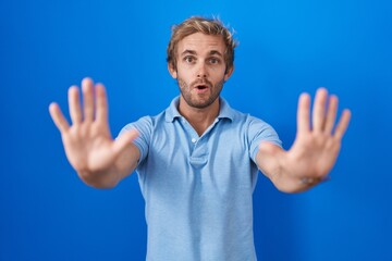 Naklejka premium Caucasian man standing over blue background doing stop gesture with hands palms, angry and frustration expression