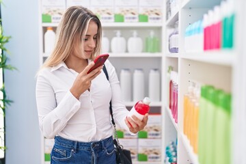 Young blonde woman customer make phot by smartphone to medicine bottle at pharmacy