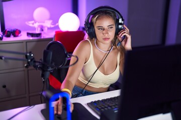 Young blonde woman streamer sitting on table with relaxed expression at gaming room