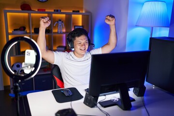 Young chinese man streamer playing video game with winner expression at gaming room
