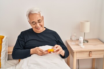 Senior man taking pills treatment sitting on bed at bedroom