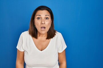 Fototapeta na wymiar Hispanic mature woman standing over blue background afraid and shocked with surprise expression, fear and excited face.