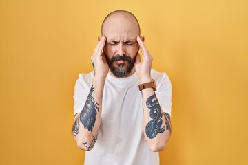 Young hispanic man with tattoos standing over yellow background with hand on head, headache because stress. suffering migraine.