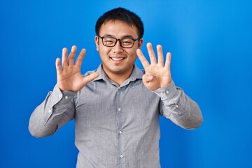 Young chinese man standing over blue background showing and pointing up with fingers number nine...