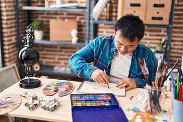 Fototapeta premium Young chinese man artist drawing on notebook at art studio