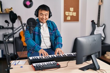 Fototapeta na wymiar Young chinese man singer singing song playing piano keyboard at music studio