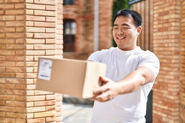 Young chinese man courier holding package at street