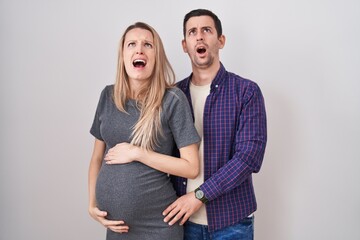 Young couple expecting a baby standing over white background angry and mad screaming frustrated and...