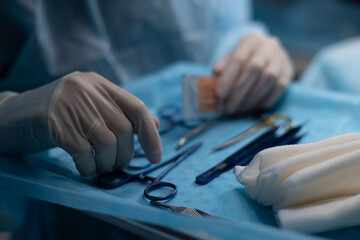 The assistant stands near the table with surgical instruments in the operating room. On the table on a blue background lie sterile surgical instruments in the operating room.