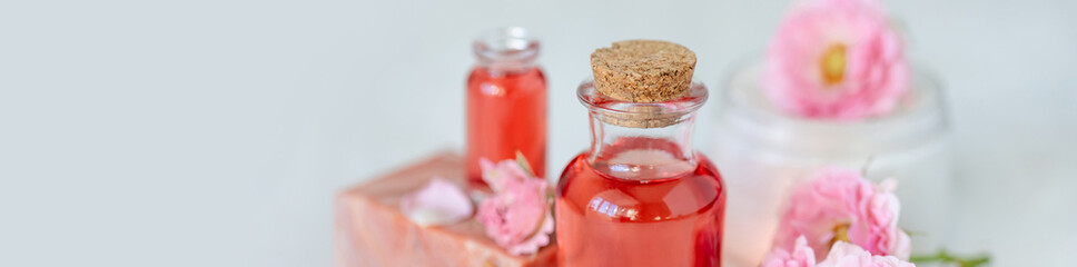 Composition with pure natural organic rose essential oil in glass bottle, luxury perfumery ingredient for fragrance, skin care products, anti-age beauty treatment. Fresh flowers banner copy space text