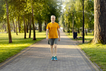 Relaxed Caucasian gray haired bearded senior athletic man walking at the park alley