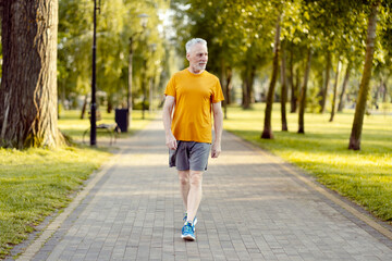 Senior athletic man walking at the park alley, preparing for the morning training