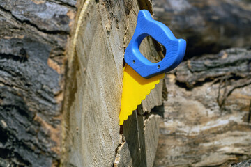 blue and yellow hand saw sawing a large tree - obrazy, fototapety, plakaty