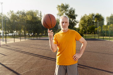 Fototapeta premium Confident handsome senior man playing basketball, spinning ball on one finger