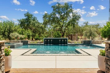 Luxury T shaped swimming pool with with a Jacuzzi and fountains surrounded by trees and a small...
