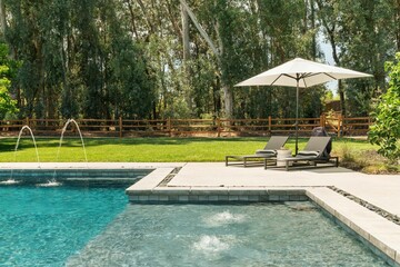 Swimming pool with fountains and two lounge chairs with an umbrella beside it