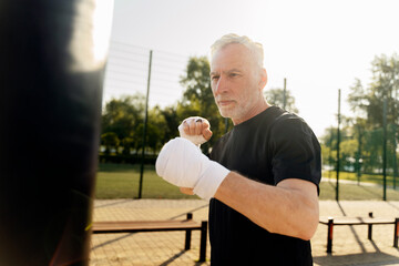 Active senior man, wearing elastic bands on wrists, boxing with punching bag