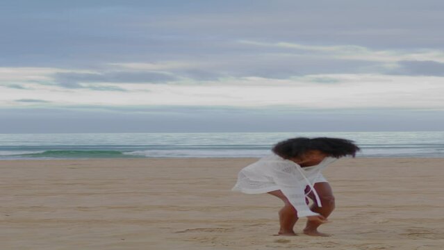 Smiling woman running ocean beach vertically. Cheerful black haired girl dancing