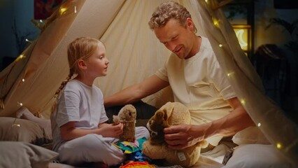 Loving caring father plays with little daughter in Indian wigwam, illuminated with beautiful lights