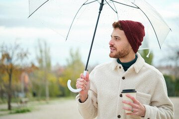 Man with a coffee and transparent umbrella in winter.