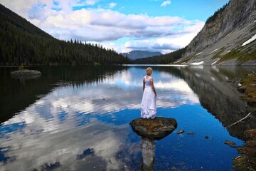 Woman on rock in the mountain lake with reflections. Kananaskis, Peter Lougheed park. Canadian Rockies. Canmore. Canada