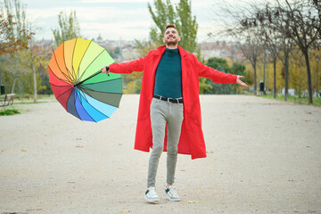 Latin young man with a red coat breathing while holding a rainbow umbrella.