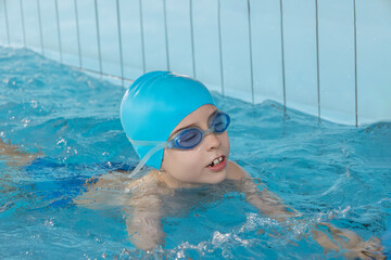 Close up boy swimmer o school boy learning how to swim in a pool wearing in swimming cap and goggles