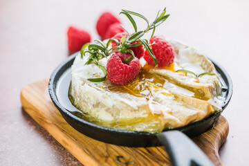 Oven baked camembert cheese with rosemary leaves and raspberry. Homemade grilled brie on rustic...