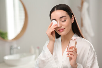 Beautiful woman removing makeup with cotton pad indoors