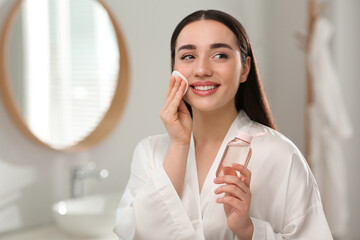 Beautiful woman removing makeup with cotton pad indoors